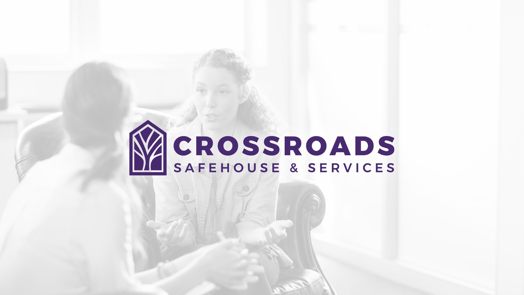 Two people talk in a bright room, with the Crossroads Safehouse & Services logo and text prominently displayed in the foreground.