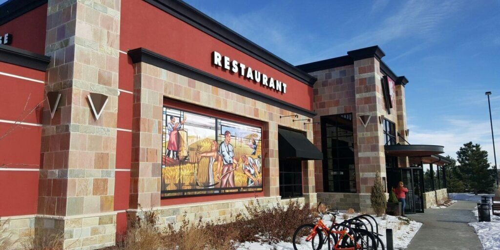 Exterior of a restaurant with a mural depicting people harvesting crops, a bike rack with bikes in front, and patches of snow on the ground.