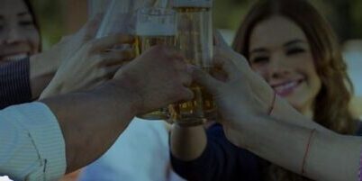 A group of people outdoors raising glasses and toasting together, smiling and enjoying a social gathering.
