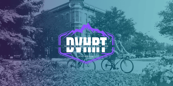 Two people ride bicycles past a historic building on a sunny day. The text “DVHRT Domestic Violence High Risk Team” is prominently displayed over the image.