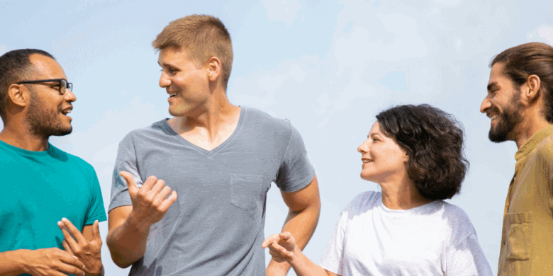 Four adults stand outdoors, engaged in conversation and smiling, with a clear sky in the background.