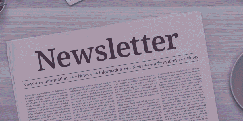 A newspaper titled "Newsletter" on a wooden table next to a cup of coffee and office supplies.